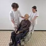 Deux étudiants soignent un mannequin en fauteuil roulant.